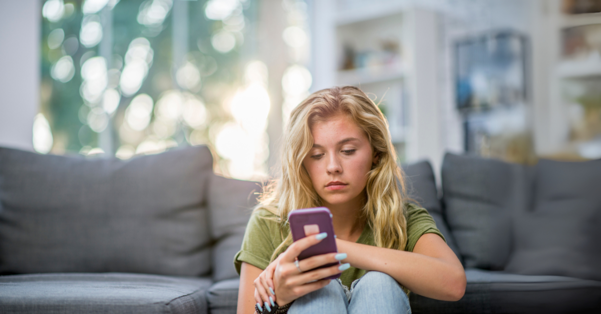 Žena sediaca v obývačke s mobilom v ruke, s očami plnými smútku, ktorá vyjadruje pocit čakania, neistoty a emocionálneho vyčerpania z dlhého písania bez skutočného stretnutia.